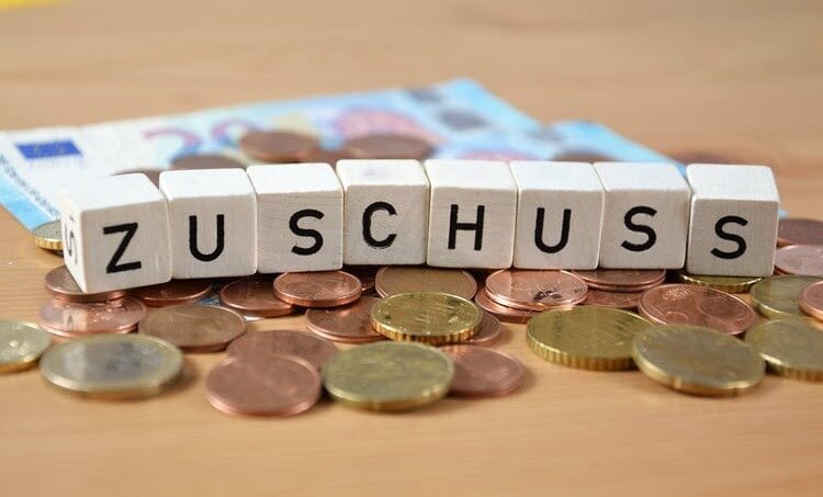 Würfel mit Buchstaben bilden das Wort Zuschüsse und liegen auf einem Haufen Kleingeld