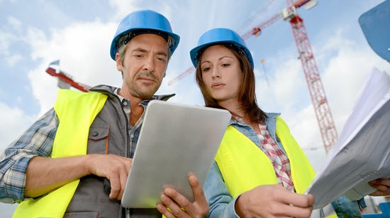 Eine Frau und ein Mann mit Schutzweste und Helm auf der Baustelle mit einem Tablet.