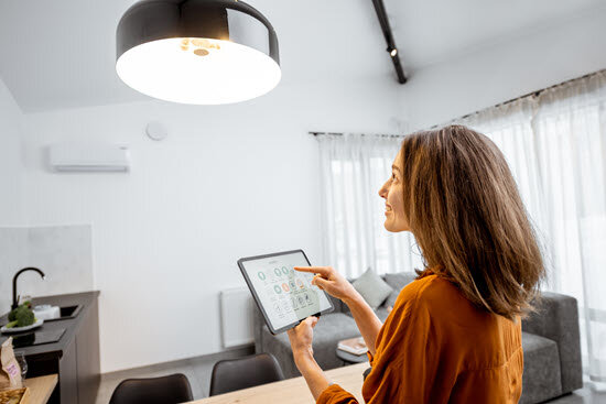 Frau guckt auf Deckenlampe während sie ein Tablet in der Hand hält um die Beleuchtung zu steuern.