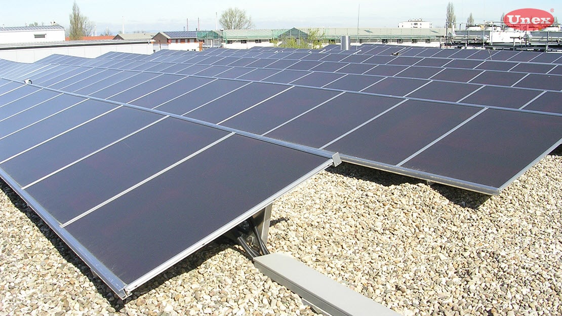 Abbildung von Solarmodulen angeschlossen über Leitungsführungssysteme auf einem Flachdach mit Kieselbelag. | © Unex
