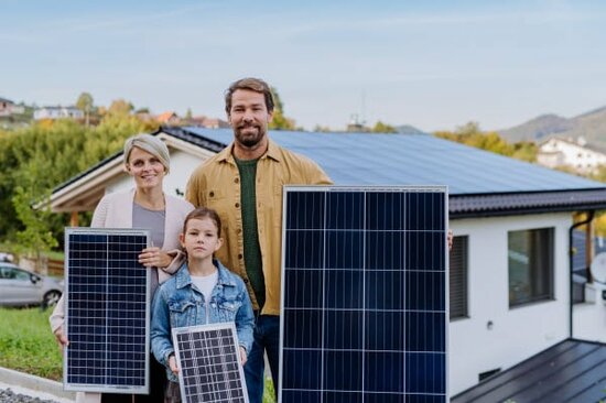 Eltern mit Kind stehen vor ihrem Haus mit verschiedenen Solarmodulen. | © 2022 Halfpoint/Shutterstock.