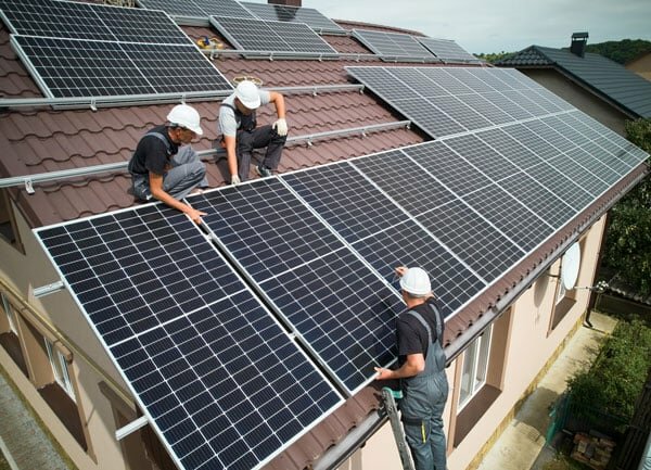 Arbeiter bringen Solarmodule auf Hausdach an. | © 2022 anatoliy_gleb/Shutterstock.